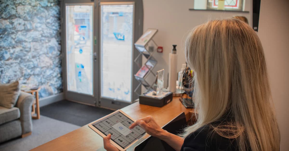 Hotel front-desk agent looking at a tablet showing a new guest feedback alert in a warm boutique hotel lobby